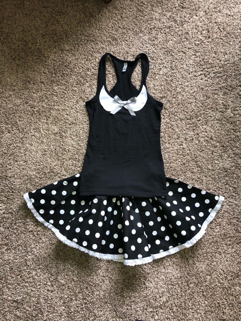 May include: A black tank top with a white collar and a white bow. The tank top is paired with a black and white polka dot skirt with a white lace trim.