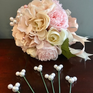 May include: A bouquet of pink and cream artificial flowers with pearl accents and a pink satin ribbon.  Six green stems with pearl accents are also included.