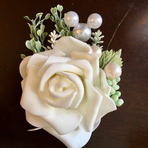 May include: A white foam rose with green leaves and pearl accents, including a Mickey Mouse head made of pearls.
