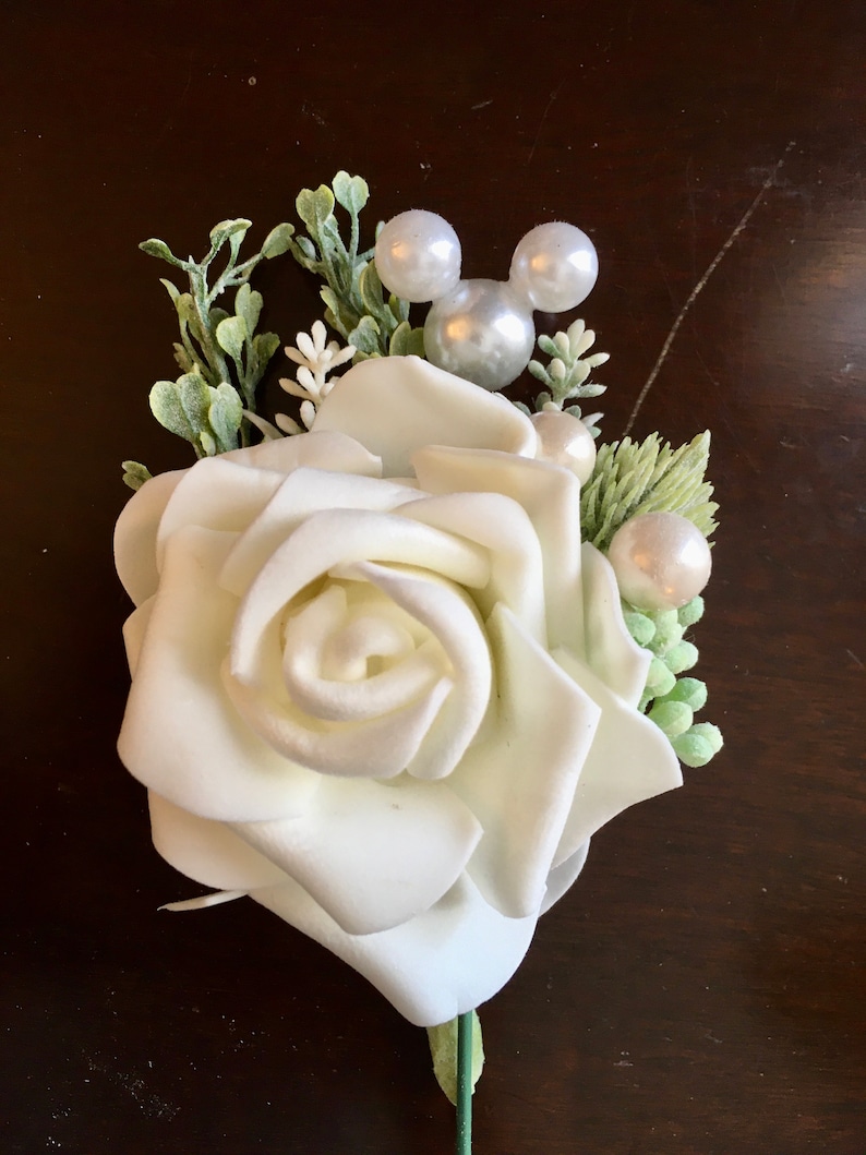 May include: A white foam rose with green leaves and pearl accents, including a Mickey Mouse head made of pearls.