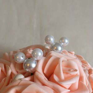 May include: A bouquet of peach-colored artificial roses with white pearl accents. The pearls are arranged in a Mickey Mouse shape.