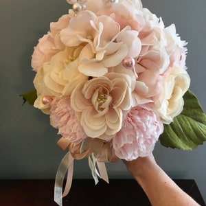 May include: A bouquet of pink and white silk flowers with pearl accents. The bouquet is tied with a satin ribbon.