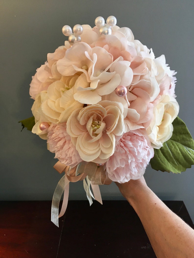 May include: A bouquet of pink and white silk flowers with pearl accents. The bouquet is tied with a satin ribbon.