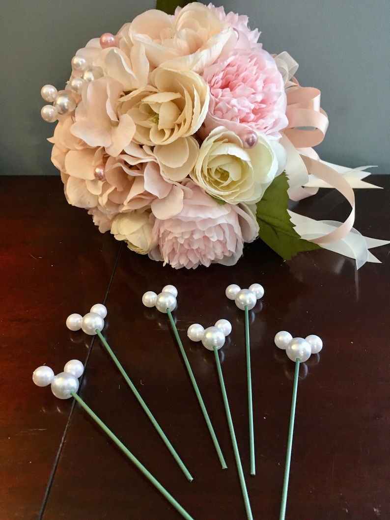May include: A bouquet of pink and cream artificial flowers with pearl accents and a pink satin ribbon.  Six green stems with pearl accents are also included.