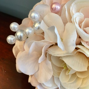 May include: A bouquet of white and blush pink artificial flowers with pearl and pink beads for decoration.