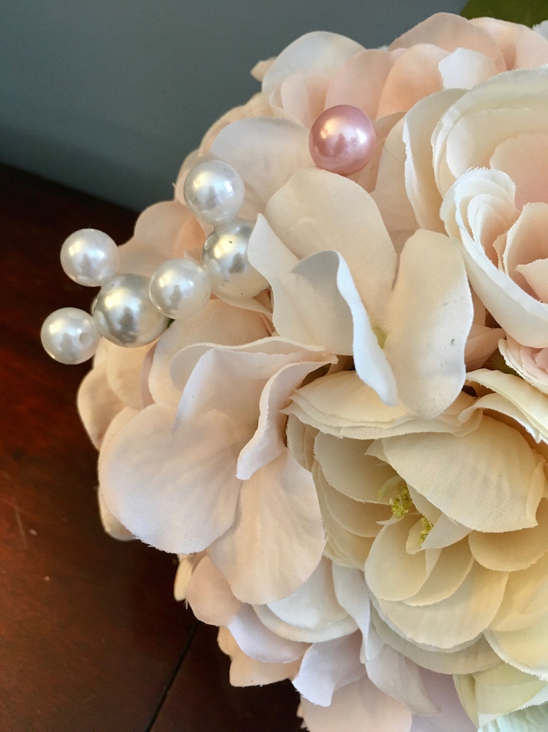 May include: A bouquet of white and blush pink artificial flowers with pearl and pink beads for decoration.