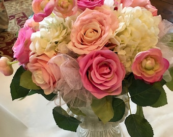 May include: A white ceramic vase with a pink and white floral arrangement. The arrangement includes roses, hydrangeas, and other pink flowers.