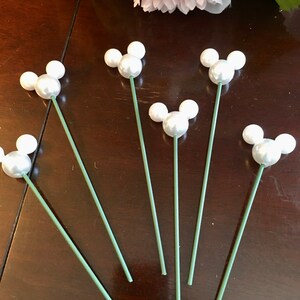 May include: Six white pearl Mickey Mouse head floral picks with green stems.