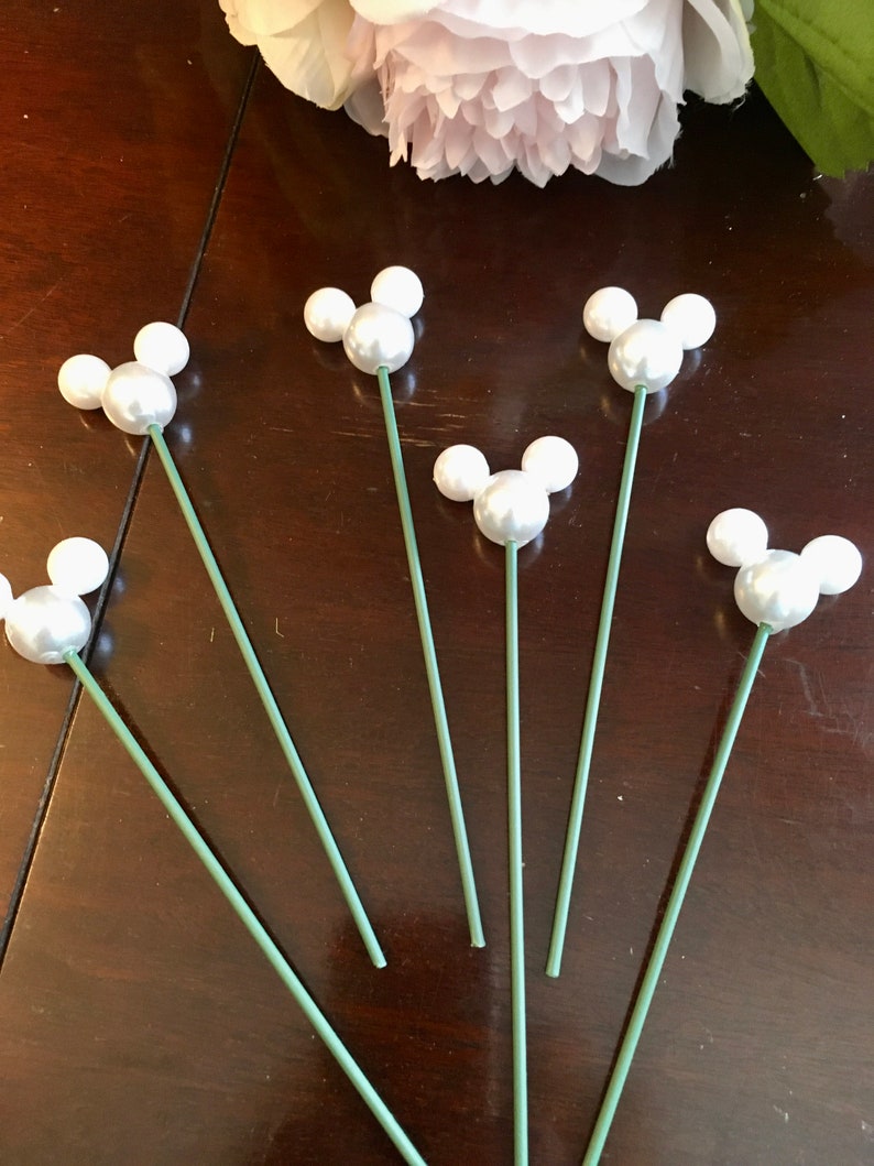 May include: Six white pearl Mickey Mouse head floral picks with green stems.
