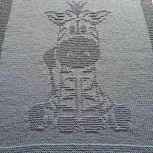 Pode incluir: Uma manta de malha azul com um design de malha branca de um robô com uma coroa na cabeça.
