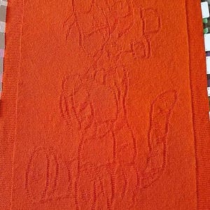 May include: Orange knitted blanket with a design of three stylised flowers.