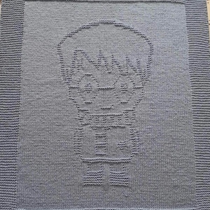 May include: A knitted blanket in shades of gray, featuring a cartoon character design. The blanket has a detailed border and a central image of a figure with glasses and a scarf. The design is created with varying stitch patterns.