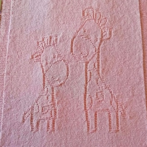 May include: A pink knitted baby blanket with a design of two giraffes. The giraffes are outlined in a lighter shade of pink.