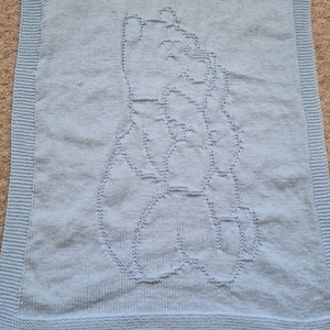 May include: A light blue knitted baby blanket with a raised design of two hands holding a heart.
