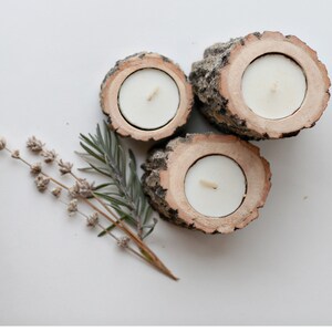 Pu&ograve; includere: Tre portacandele in legno rustico con candele tealight bianche. I portacandele sono realizzati in corteccia d'albero e hanno una finitura in legno naturale.