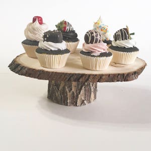 May include: A wooden cake stand with a tree bark design, featuring six cupcakes with various toppings, including chocolate, sprinkles, and strawberries.