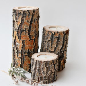 Pu&ograve; includere: Tre portacandele in legno realizzati con corteccia d'albero con candele bianche all'interno. I portacandele sono disposti a forma di piramide.
