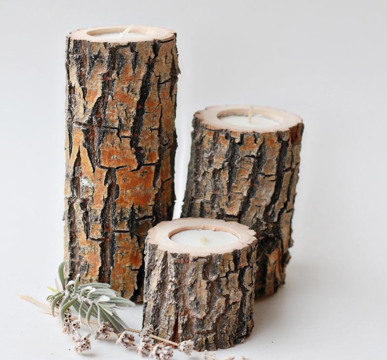 Pu&ograve; includere: Tre portacandele in legno realizzati con corteccia d'albero con candele bianche all'interno. I portacandele sono disposti a forma di piramide.