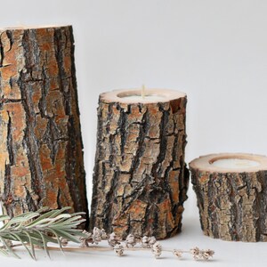 Pu&ograve; includere: Tre portacandele in legno rustico realizzati con corteccia d'albero. I portacandele sono di dimensioni diverse e hanno una finitura in legno naturale.