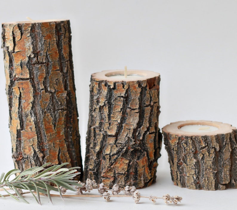 Pu&ograve; includere: Tre portacandele in legno rustico realizzati con corteccia d'albero. I portacandele sono di dimensioni diverse e hanno una finitura in legno naturale.