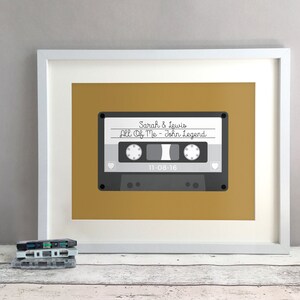 May include: A framed print of a cassette tape with the text "Sarah & Lewis All Of Me - John Legend 11-08-16" on a mustard yellow background.