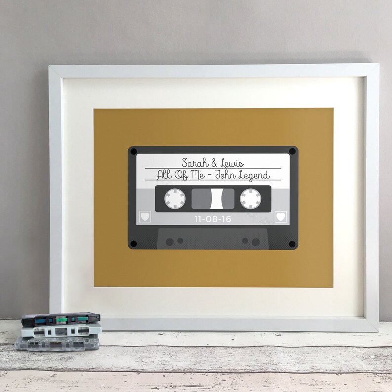 May include: A framed print of a cassette tape with the text "Sarah & Lewis All Of Me - John Legend 11-08-16" on a mustard yellow background.