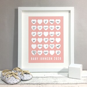 May include: A white frame with a pink background and white hearts. Each heart has a handwritten name inside. The text at the bottom of the frame reads "BABY JOHNSON 2020".