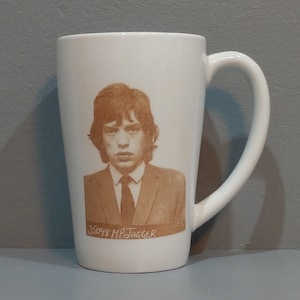 May include: White ceramic mug with a brown image of Mick Jagger. The mug has a handle and the text "35098 MJAGGER" is printed on the bottom of the image.