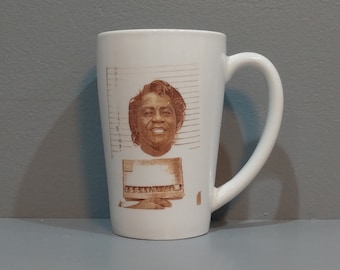 May include: White ceramic mug with a brown image of a man's face with a mugshot background. The mugshot background has a height chart and the text "16541144".