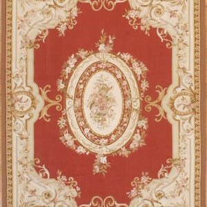 Może przedstawiać: Prostokątny dywan z czerwonym centralnym polem, obramowany kremową obwódką z kwiatowymi i kręconymi wzorami. Dywan posiada owalny kwiatowy medalion pośrodku i kwiatowe akcenty. Wymiary nie są widoczne.