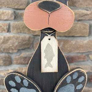 May include: A wooden bear figurine with a black body, a pink nose, and gray paw prints. The bear has a tag with a fish silhouette. The figurine is painted with a distressed finish, giving it a rustic look.
