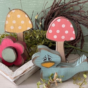 May include: A set of wooden spring-themed decorations featuring a blue bird, a pink mushroom with white polka dots, a yellow mushroom with white polka dots, and a pink flower with a green center.