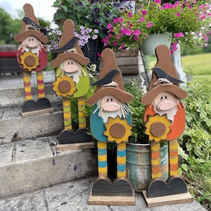 Peut inclure: Quatre figurines de gnomes en bois avec des visages, des chapeaux et des tournesols peints. Chaque gnome est peint dans une couleur différente : rouge, vert, bleu et orange. Les gnomes sont debout sur des bases en bois.