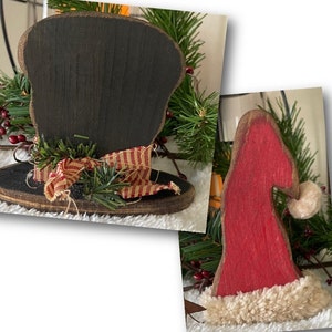May include: Wooden Christmas decorations featuring a black top hat with a red and white striped bow and a red Santa hat with a white pom-pom and trim. The hats are rustic and festive, perfect for holiday decor.