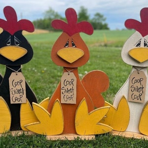 Könnte beinhalten: Drei hölzerne Hühnerfiguren mit gelben Füßen, roten Kämmen und braunen, schwarzen und weißen Körpern. Jedes Huhn hat ein braunes Schild mit der Aufschrift "Coop Sweet Coop".