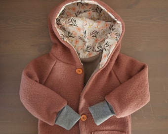 May include: A dusty rose hooded jacket featuring a floral patterned lining with pink flowers and dark leaves. The jacket has long sleeves with grey ribbed cuffs and two orange buttons down the front center. The hood is large and structured.