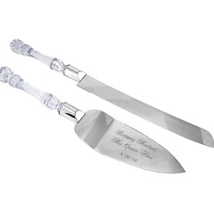 May include: A set of two silver cake cutting knives with clear plastic handles. The larger knife has a serrated edge and the smaller knife has a rounded edge. The smaller knife is engraved with the text "Brittany Martinez, Miss Quince Anos, 8/20/18".
