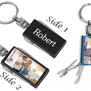 May include: A silver multi-tool keychain with a black and blue rectangular insert. One side of the insert has a photo of a family, and the other side has the name "Robert" engraved on it.