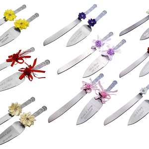 May include: Set of two silver cake knives with decorative handles. The handles are adorned with various colored flowers and ribbons. The knives are engraved with names and dates.