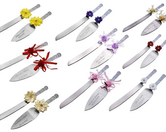May include: Set of two silver cake knives with decorative handles. The handles are adorned with various colored flowers and ribbons. The knives are engraved with names and dates.