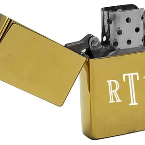 May include: A gold-colored lighter with a hinged lid. The lighter has a white inscription that reads "RTL".