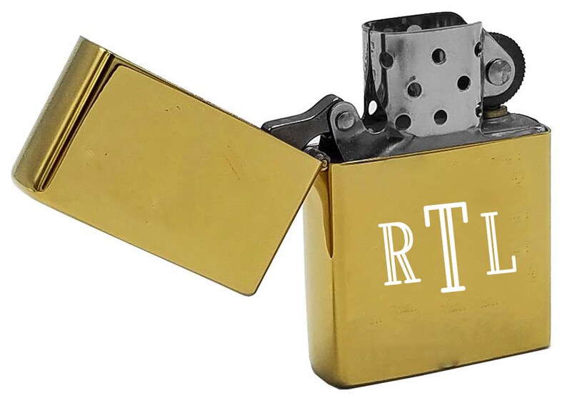 May include: A gold-colored lighter with a hinged lid. The lighter has a white inscription that reads "RTL".