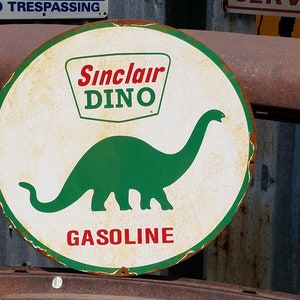 Op de afbeelding: Een vintage Sinclair Dino benzinebord met een groen dinosaurus silhouet en de tekst "Sinclair Dino Gasoline".