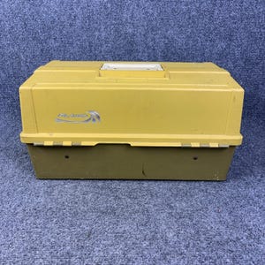 May include: A rectangular Plano tackle box featuring a two-tone design with a mustard yellow lid and a dark olive green base. The lid includes a recessed handle and the silver Plano logo printed on the front. The box has a hinged construction.
