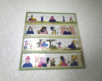 Op de afbeelding: Een set van vier antieke handgeschilderde glazen dia's, elk met een groen houten frame. De dia's tonen verschillende figuren in historische kleding, waaronder een vrouw in een gele jurk en een man in een blauwe jas.