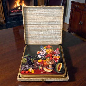 May include: A set of decorative coasters featuring a still life of flowers and fruit. The coasters are in a rectangular box with a light wood grain pattern. The artwork on the coasters includes grapes, lemons, and a variety of colorful flowers.