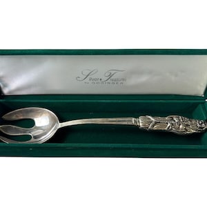 Könnte beinhalten: Silberne Serviergabel mit dekorativem Griff, präsentiert in einer grünen Samtbox mit Satinfutter. Die Gabel hat ein Design mit drei Zinken. Die Box trägt den Text "Silver Treasures by Godinger".