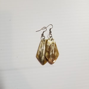 Può includere: Un paio di orecchini con un design a motivi marroni e bianchi. Gli orecchini sono in corno e hanno ganci d'argento.