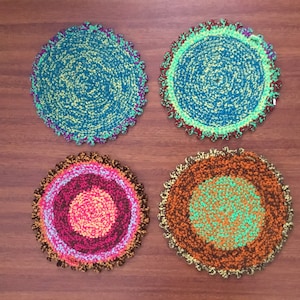 May include: Four crocheted round placemats in different colors and patterns. The placemats are made with a variety of yarns in shades of green, blue, orange, pink, and brown.