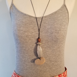 May include: A simple necklace with a brown, white, and gray stone pendant. The necklace is made of a black cord and is worn on a gray tank top.